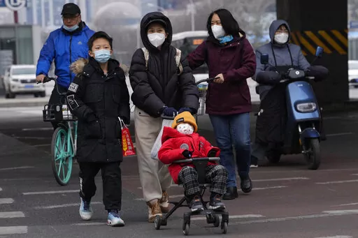 A child wearing a mask is pushed across a road in Beijing, Friday, Dec. 2, 2022. More cities eased restrictions, allowing shopping malls, supermarkets and other businesses to reopen following protests last weekend in Shanghai and other areas in which some crowds called for President Xi Jinping to resign. (AP Photo/Ng Han Guan)
