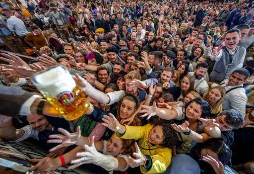 Young people reach out for free beer in one of the beer tents on the opening day of the 187th Oktoberfest beer festival in Munich, Germany, Saturday, Sept. 17, 2022. Oktoberfest is back in Germany after two years of pandemic cancellations, the same bicep-challenging beer mugs, fat-dripping pork knuckles, pretzels the size of dinner plates, men in leather shorts and women in cleavage-baring traditional dresses.  (AP Photo/Michael Probst)