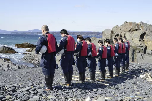 Police officers offer a silent prayer ahead of their search operation for the missing persons in Minamisanriku, Miyagi prefecture, northern Japan Monday, March 11, 2024. Japan marked the 13th anniversary of the massive earthquake, tsunami and nuclear disaster. (Kyodo News via AP)