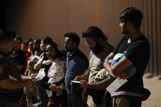 Migrants wait to be processed by Border Patrol agents near the end of a border wall Tuesday, Aug. 23, 2022, near Yuma, Arizona. The Border Patrol is seeing a dramatic shift in the type of migrants who come across the busiest places on the U.S.-Mexico. Migrants are now coming from more than 100 countries, and Mexicans are virtually absent. (AP Photo/Gregory Bull)