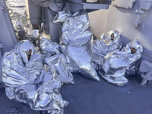 In this photo provided by the Greek Coast Guard, some of the nine men who survived a shipwreck and were found on an uninhabited islet are covered with a thermal blankets as they sit aboard a Greek Coast guard vessel, in the Aegean Sea, Greece, on Tuesday, Nov. 1, 2022. A major search and rescue operation was underway Tuesday for dozens of people missing after the boat they were on capsized and sank in stormy weather overnight off the coast of an island near the Greek capital. The coast guard sai