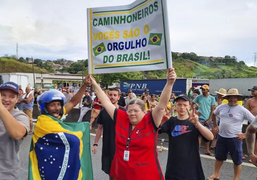 A resident holds a sign that reads in Portuguese: "Truck drivers, you are the pride of Brazil" to show support for cargo drivers who parked their trucks on the side of the Rio de Janeiro-Sao Paulo highway to protest the previous day’s election defeat of President Jair Bolsonaro, in Barra Mansa, Rio de Janeiro state, Brazil, Monday, Oct. 31, 2022. (AP Photo/Rodrigues Da Silva)