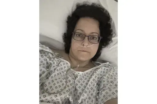 This July 2023 self-portrait provided by Anna Gittins shows the elementary school principal from Hereford in western England in a hospital bed during her cancer treatment. Gittins was shocked when she found out she had advanced colorectal cancer in 2022. But when she contacted her local hospital, she was told no one would be able to see her for three months "due to high demand and low capacity of senior doctors." Gittins had access to private health care and has since undergone surgery and chemo