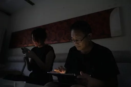 Wang Quanzhang and his wife Li Wenzu look at their phone and laptop in the dark after power was cut off for their apartment in Beijing's Changping district, Tuesday, June 20, 2023. Disbarred human rights lawyer Wang Quanzhang has been forced to move 13 times in two months as part of a pattern of harassment against him and three other prominent rights advocates in Beijing that is further squeezing the country's battered civil rights community. (AP Photo/Ng Han Guan)