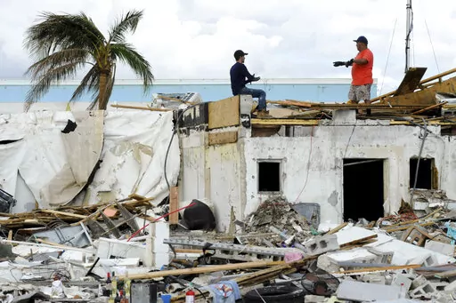 Workers talk atop a building that was heavily damaged by Hurricane Ian at Fort Myers Beach, Fla., on Sunday, Oct. 9, 2022. (AP Photo/Jay Reeves)