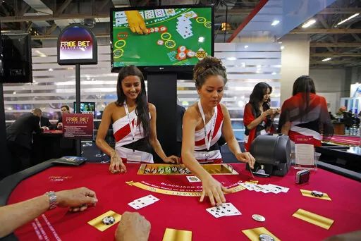 Attendants conduct play with the visitors over a Black Jack gaming table during the Global Gaming Expo Asia in Macao, May 23, 2013. Losing money due to COVID, the American casino giants that helped make Macao the "Las Vegas of Asia" face a fresh challenge: The tiny Chinese territory wants them to reduce its reliance on gambling by building theme parks and other tourist attractions. (AP Photo/Kin Cheung, File)