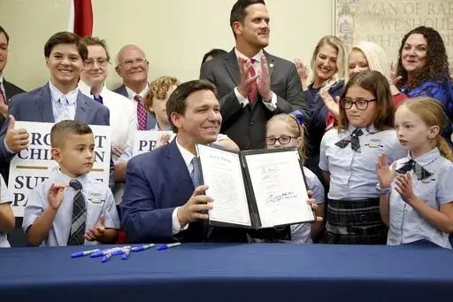 Florida Gov. Ron DeSantis displays the signed Parental Rights in Education, aka the Don't Say Gay bill, flanked by elementary school students during a news conference on Monday, March 28, 2022, at Classical Preparatory school in Shady Hills. (Douglas R. Clifford/Tampa Bay Times via AP)