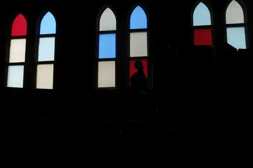 A woman is silhouetted against the stained-glass windows at the Ryman Auditorium, known as the Mother Church of Country music, in Nashville, Tenn., on July 30, 2024. (AP Photo/Luis Andres Henao)