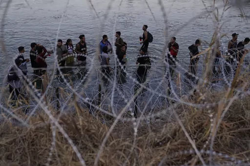 Migrants wait to climb over concertina wire after they crossed the Rio Grande and entered the U.S. from Mexico, Saturday, Sept. 23, 2023, in Eagle Pass, Texas. Abbott is expected to sign into law sweeping new powers that allow police to arrest migrants who cross the border illegally and gives local judges authority to order them to leave the country. (AP Photo/Eric Gay, File)