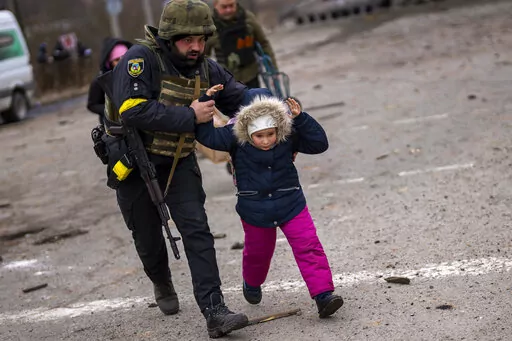 A Ukrainian police officer runs while holding a child as the artillery echoes nearby, while fleeing Irpin on the outskirts of Kyiv, Ukraine, Monday, March 7, 2022. (AP Photo/Emilio Morenatti)