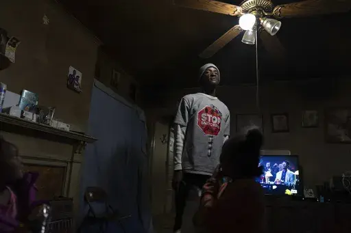 Tyrone Heard stands in his living room with his kids Karinina, 8, Tyrone, Jr., 7, and Kylee, 5, after they arrived home from school, Friday, Dec. 6, 2024, in Alexander City, Ala. Heard's uncle, Willie Craytwon was killed while on work release riding in an Alexander City Work Center transport van that crashed in April. (AP Photo/Carolyn Kaster)