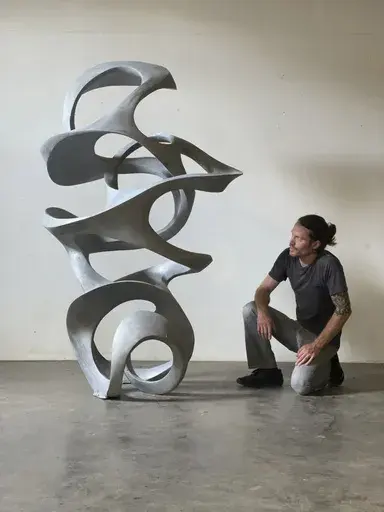 In this photo provided by Jacob Burmood, the artist poses for a portrait with one of his sculptures entitled "Current Sequence" in Kansas City, Mo., July 2021. (Jacob Burmood via AP)