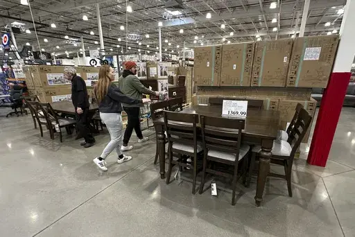 Shoppers pass by a dining room set on display in a Costco warehouse Thursday, Jan. 23, 2025, in Sheridan, Colo. (AP Photo/David Zalubowski)