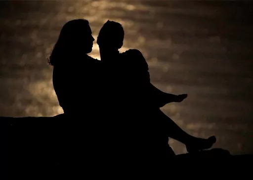 In this June 27, 2018, file photo a couple is silhouetted against moonlight reflecting off the Missouri River as they watch the full moon rise beyond downtown buildings in Kansas City, Mo. Money can create stress within a relationship, but talking through expectations and money beliefs can help couples get on the same page. In fact, conflict over money can be healthy, partly because we often partner with people who are our financial opposites. (AP Photo/Charlie Riedel, File)