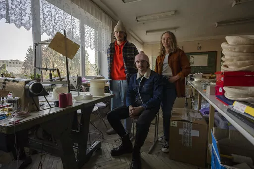 Ukrainian co-founders of high-end hat designer brand Ruslan Baginskiy 'RB', from left, public relations director Petro Yasinskiy, designer and creative director Ruslan Baginskiy and Victoria Semerei, whole sale director, pose for a photograph, inside a college classroom turned into a workshop they have been working from after fleeing Kiev, in Lviv, western Ukraine, Friday, March 25, 2022. Daily bombings led the company's co-founders to make the decision to flee. (AP Photo/Nariman El-Mofty)