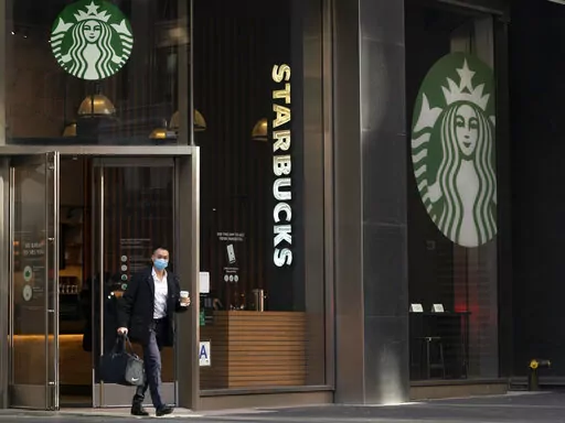 A man carries a beverage as he walks out of a Starbucks coffee shop, Tuesday, Jan. 19, 2021, in New York. Companies that would be affected by a Biden administration vaccine-or-testing requirement for workers remain on the sidelines while the Supreme Court considers whether the rule can be enforced. Since then, Starbucks has announced its own vaccine mandate saying in Dec. 2021, that all U.S. workers must be fully vaccinated by Feb. 9, 2022, or face a weekly COVID testing requirement. (AP Photo/M