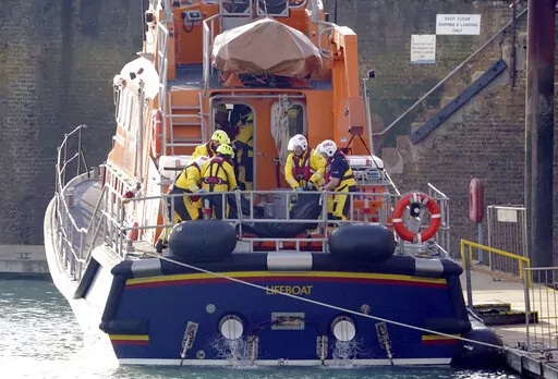 Members of the Dover lifeboat place a body bag on a stretcher after returning to the Port of Dover after a large search and rescue operation launched in the Channel off the coast of Dungeness, in Kent, Wednesday Dec. 14, 2022, following an incident involving a small boat likely to have been carrying migrants. Helicopters and lifeboats have been dispatched to the English Channel off the coast of Kent in southern England to rescue a small boat in distress, authorities said Wednesday. (Gareth Fulle