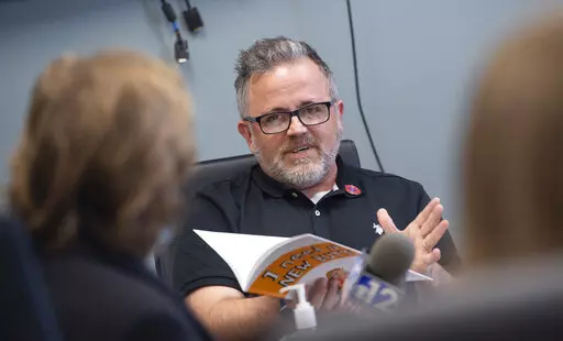 Toby Price, a former assistant principal at Gary Road Elementary School in Byram, Miss., testifies during an appeal hearing at the Hinds County Schools administration building in Raymond, Miss., Monday, March 28, 2022, regarding his dismissal after reading the children's book he's holding, "I Need a New Butt!" by Dawn McMillan. Price told the Clarion Ledger he received a 12-page order Monday, May 11, 2022, showing the Hinds County School Board had voted 2-1 to uphold the superintendent's decisio