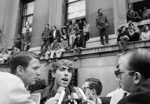 Mark Rudd, a leader of the student protest at Columbia University in New York City, is interviewed outside Low Memorial Library, background, April 25, 1968, which has been occupied by students since the previous day. Rudd said the purpose of the protest was to "hit at" what he claimed was the university's policy of "racism and support for imperialism." (AP Photo/File)