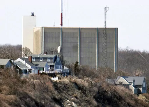 A portion of the Pilgrim Nuclear Power Station is visible beyond houses along the coast of Cape Cod Bay, in Plymouth, Mass., March 30, 2011. Pilgrim, which closed in 2019, was a boiling water reactor. Water constantly circulated through the reactor vessel and nuclear fuel, converting it to steam to spin the turbine. The water was cooled and recirculated, picking up radioactive contamination. (AP Photo/Steven Senne, File)