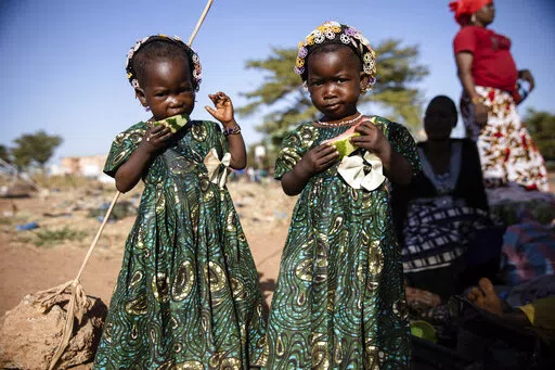 Twins eat slices of watermelon Thursday Nov. 25, 2021 at the Patte d'Oie district of Ouagadougou, Burkina Faso, where mothers of twins come to beg on the road. In Burkina Faso, a country with a strong belief in the supernatural, twins are regarded as children of spirits whose mothers were specially selected to bear them. (AP Photo/Sophie Garcia)