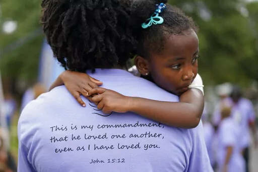 Nikiesha Thomas' cousin Paul McLeod holds his daughter Blair McLeod during a Back To School Block Party in the Robinwood Community of Annapolis, Md., Sunday, Aug. 21, 2022, in honor of Nikiesha. Nikiesha posted the Bible verse John 15:12 on social media the day she was shot and killed by her ex-boyfriend just days after filing for a protective order. The verse is seen printed on Paul's T-shirt. Victims of abuse and their families saw a quiet breakthrough this summer when the passage of a biparti