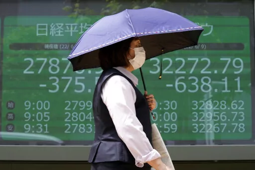 A woman wearing a protective mask in front of an electronic stock board showing Japan's Nikkei 225 and New York Dow indexes at a securities firm Friday, June 10, 2022, in Tokyo. Shares were mostly lower in Asia on Friday, with only Shanghai rising, after stocks tumbled on Wall Street on expectations central banks will focus on battling inflation with interest rate hikes. (AP Photo/Eugene Hoshiko)