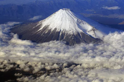 In this Dec. 8, 2010 file photo, snow-covered Mount Fuji, Japan's highest peak at 3,776-meters tall (12,385 feet), is seen from an airplane window. Those who want to climb one of the most popular trails of the iconic Japanese Mount Fuji will now have to reserve ahead and pay a fee as the picturesque stratovolcano struggles with overtourism, littering and those who attempt rushed “bullet climbing,” putting lives at risk. (AP Photo/Itsuo Inouye, File)
