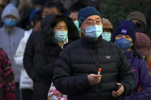 A man wearing a face mask holds his testing tube as masked residents line up for their routine COVID-19 throat swabs at a coronavirus testing site in Beijing, Sunday, Dec. 4, 2022. China on Sunday reported two additional deaths from COVID-19 as some cities move cautiously to ease anti-pandemic restrictions amid increasingly vocal public frustration over the measures. (AP Photo/Andy Wong)