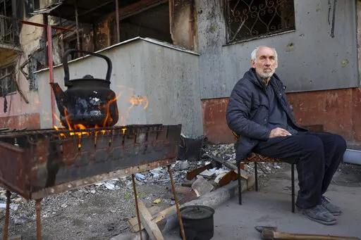 A local man sits in front of an apartment building damaged from heavy fighting as he waits for the kettle to boil in an area controlled by Russian-backed separatist forces in Mariupol, Ukraine, Tuesday, April 26, 2022. (AP Photo/Alexei Alexandrov)