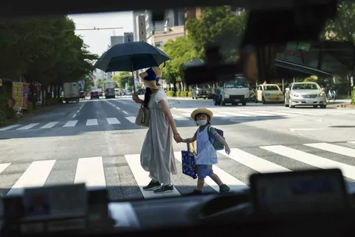 A pedestrian crossing a street with a child is seen through a taxi window in Tokyo, Monday, July 19, 2021. The number of babies born in Japan last year fell for an eighth straight year to a new low, government data showed Tuesday, Feb. 27, 2024, and a top official said it was critical for the country to reverse the trend in the coming half-dozen years. (AP Photo/David Goldman, File)