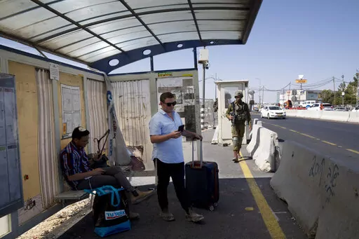 An Israeli soldier patrols a bus stop as settlers wait for a ride at the Gush Etzion junction, the transportation hub for a number of West Bank Jewish settlements, Thursday, June 9, 2022. Israeli settlers in the occupied West Bank may soon have a taste of the military rule that Palestinians have been living under for 55 years. A looming end-of-month deadline to extend legal protections to Jewish settlers has put Israel’s government on the brink of collapse and drawn widespread warnings that th