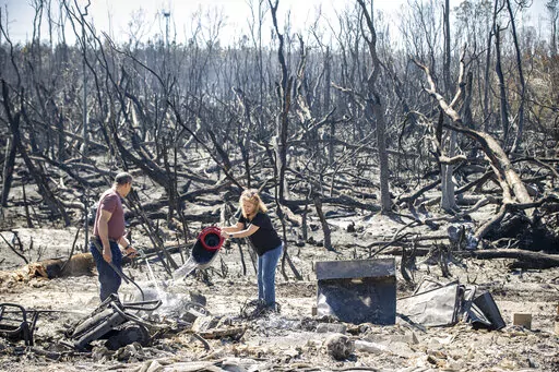 Hector Rivera and Wandi Blanco put water on hotspots behind their home in Panama City, Fla., Saturday, March 5, 2022, following a wildfire that started Friday. The fire destroyed two homes next to them and melted the siding off of their home. (Mike Fender/News Herald via AP)