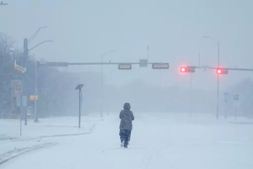 A jogger trots on a snow-covered road during a winter storm, Jan. 15, 2024, in Grand Prairie, Texas. Winter weather brings various hazards that people have to contend with to keep warm and safe. These dangers can include carbon monoxide poisoning, hypothermia and frozen pipes that can burst and make homes unlivable. Public safety officials and experts say there are multiple ways people can prepare themselves to avoid these hazards and keep themselves safe. (AP Photo/Julio Cortez, file)