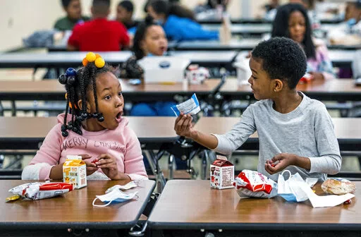 First graders, from left, Kendal Kates and Ryan Kenney are excited about the contents of their boxed lunches at Langley K-8 School, Dec. 23, 2021, in the Sheraden neighborhood in Pittsburgh. The Biden administration has issued transitional standards for school lunches that are meant to get cafeterias back on a healthier course as they recover from pandemic and supply chain disruptions.  The “bridge” rule announced by the U.S. Agriculture Department on Friday extends emergency flexibilities f