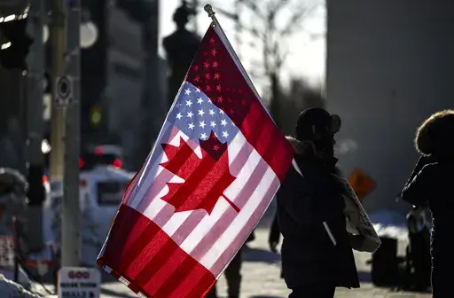 A protester holds the flags of Canada and the United States outside on Parliament Hill in Ottawa, on Saturday, Feb. 1, 2025. (Justin Tang/The Canadian Press via AP)