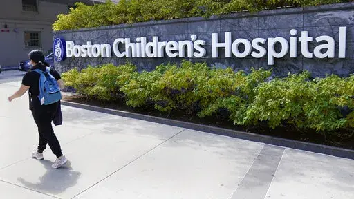 FILE — A woman walks past a sign outside the Boston Children's Hospital, Thursday, Aug. 18, 2022, in Boston. The American Academy of Pediatrics, the American Medical Association and the Children's Hospital Association are asking U.S. Attorney General Merrick Garland to investigate and prosecute people who are threatening violence against children's hospitals and physicians that provide gender-affirming health care. (AP Photo/Charles Krupa, File)