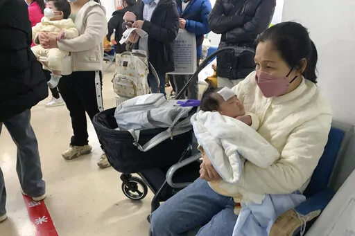 A woman tends to a child at the fever clinic of a Children's hospital in Beijing, Wednesday, Dec. 14, 2022. China's National Health Commission scaled down its daily COVID-19 report starting Wednesday in response to a sharp decline in PCR testing since the government eased antivirus measures after daily cases hit record highs. (AP Photo/Dake Kang)