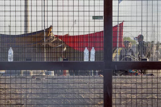 Two migrants, part of a small group, are seeing through the mesh of the border fence as they camp outside a gate in El Paso, Texas, Friday, May 12, 2023. Migrant children in makeshift camps along the U.S.-Mexico border who are waiting to be processed by Border Patrol are in the agency's custody _ something the agency had denied _ and said the Department of Homeland Security must quickly process them and place them in facilities that are “safe and sanitary.”(AP Photo/Andres Leighton, File)