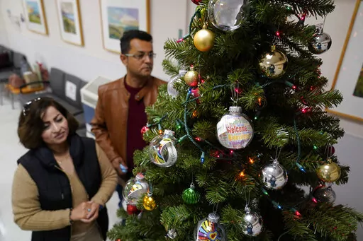 Mohammad Attaie and his wife Deena, newly arrived from Afghanistan, look over ornaments on a Christmas Tree at the Valley Health Center TB/Refugee Program in San Jose, Calif., on Dec. 9, 2021. The staff of Silicon Valley's decades-old refugee health clinic may not all speak the language of the Afghan refugees starting new lives in the San Francisco Bay Area. But they know the anxiety and stress of newcomers who fled war and chaos to end up in a country where they don't speak the language and eve