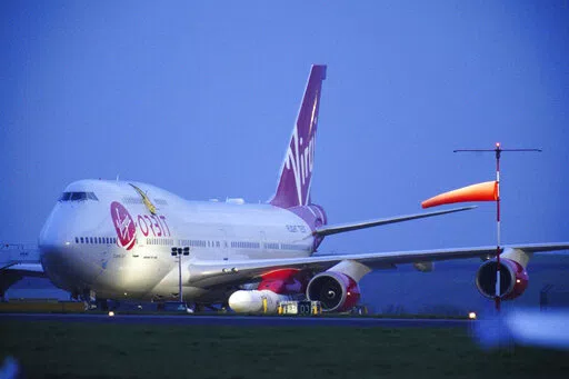 Virgin Atlantic Cosmic Girl, a repurposed Virgin Atlantic Boeing 747 aircraft carrying a rocket, is parked at Spaceport Cornwall, at Cornwall Airport in Newquay, England, Monday, Jan. 9, 2023. Engineers are making final preparations for the first satellite launch from the U.K. later Monday, when a repurposed passenger plane is expected to release a Virgin Orbit rocket carrying several small satellites into space. (Ben Birchall/PA via AP)
