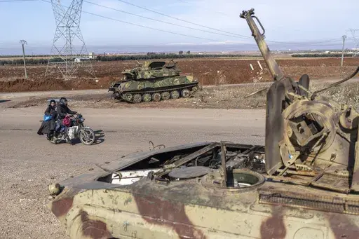 A family drives past tanks that belonged to the Assad government, in Nawa, near Daraa, Syria, Jan. 4, 2025. (AP Photo/Mosa'ab Elshamy)