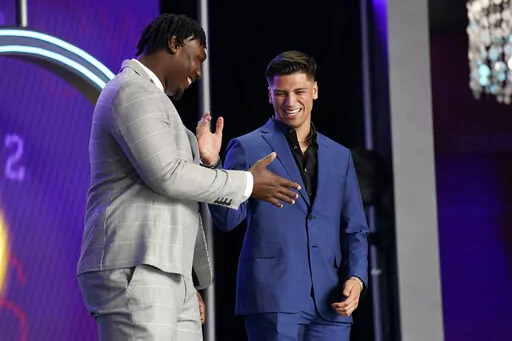 Mississippi quarterback Matt Corral, right, shakes hands with Mississippi State offensive lineman Charles Cross during the first round of the NFL football draft Thursday, April 28, 2022, in Las Vegas. (AP Photo/John Locher)