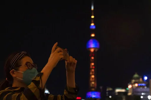 A woman takes photos near the Oriental Pearl Tower on the bund, Tuesday, May 31, 2022, in Shanghai. Shanghai authorities say they will take major steps Wednesday toward reopening China's largest city after a two-month COVID-19 lockdown that has set back the national economy and largely confined millions of people to their homes. (AP Photo/Ng Han Guan)