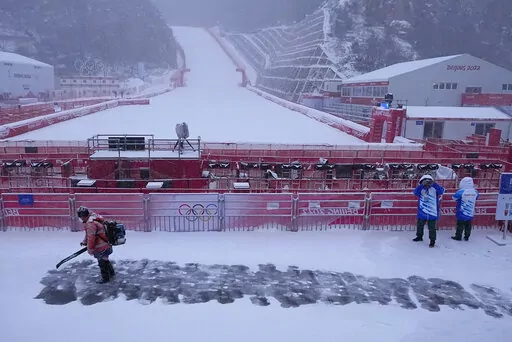 A worker clears snow from the stands in the finish area at the alpine ski venue at the 2022 Winter Olympics, Sunday, Feb. 13, 2022, in the Yanqing district of Beijing. (AP Photo/Robert F. Bukaty)