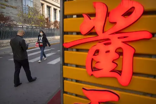 People wearing face masks walk in the Wangfujing shopping district in Beijing, Saturday, Nov. 19, 2022. Performances have been suspended at one of Beijing's oldest and most renowned theaters amid a new wave of shop and restaurant closures in response to a spike in COVID-19 cases in the Chinese capital. (AP Photo/Mark Schiefelbein)