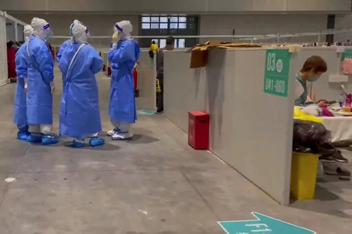 In this image taken from video provided by Beibei, who asked to be identified only by her given name, medical workers wearing protective suits chat as a resident takes a rest at the National Exhibition and Convention Center on April 15, 2022, in Shanghai.  The convention center converted to a quarantine facility set up for people who tested positive but have few or no symptoms. (Beibei via AP)