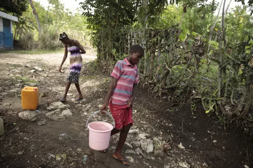 Siblings Mylouise Veillard, left, and Myson walk home with water they collected from a well, for cooking, cleaning and drinking, in a rural area of Saint-Louis-du-Sud, Haiti, Thursday, May 25, 2023. The siblings were considered “poverty orphans" for three years until they were reunited with their mother, Renèse Estève, who had dropped them off at an orphanage where she believed they'd get better care. Their mother brought them home after she was startled at the weight they had lost, convince