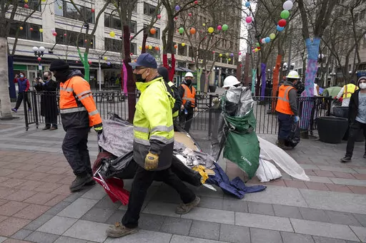 Workers carry a tent used by people experiencing homelessness to a garbage truck, Friday, March 11, 2022, during the clearing and removal of several tents at an encampment in Westlake Park in downtown Seattle. Increasingly in liberal cities across the country — where people living in tents in public spaces have long been tolerated — leaders are removing encampments and pushing other strict measures to address homelessness that would have been unheard of a few years ago. (AP Photo/Ted S. Warr