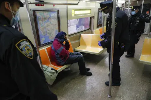New York Police Department officers wake up sleeping passengers and direct them to the exits at the 207th Street station on the A train, Thursday, April 30, 2020, in the Manhattan borough of New York. In New York City's latest effort to address a mental health crisis on its streets and subways, Mayor Eric Adams announced Tuesday, Nov. 29, 2022, that authorities would more aggressively intervene to help people in need of treatment, saying there was "a moral obligation" to do so, even if it means 